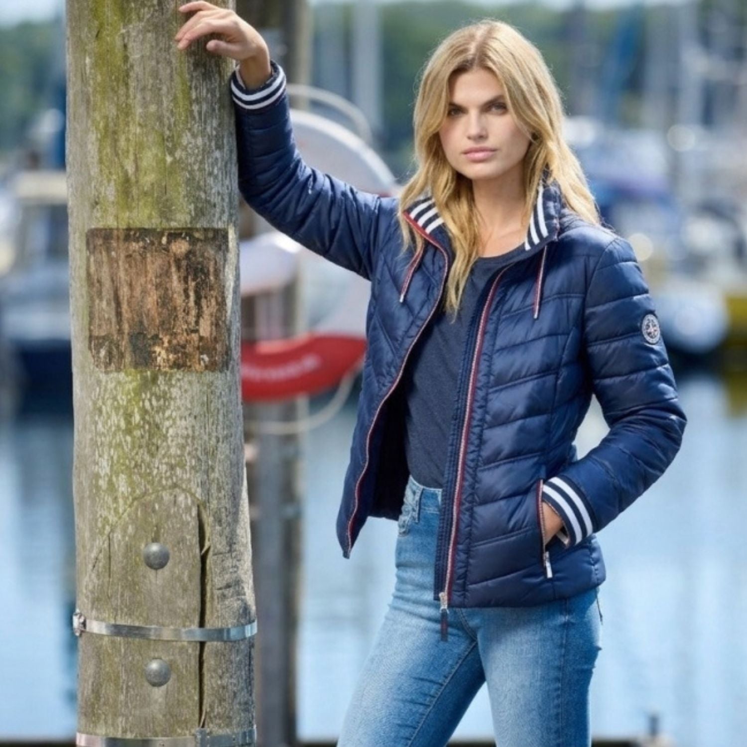 Woman in navy quilted summer jacket with striped rib cuffs at a harbour showing summer jacket trends 2026.